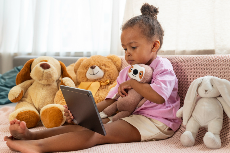 toddler girl surrounded by stuffed animals and using an ipad