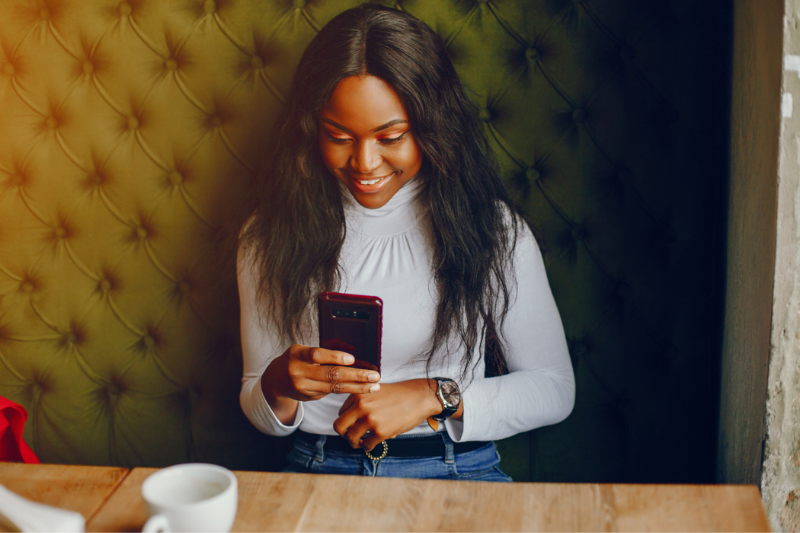 smiling woman sitting at a table looking at her phone with a coffee cup in front of her